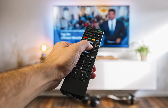 hand med fjärrkontroll till tv i bakgrunden