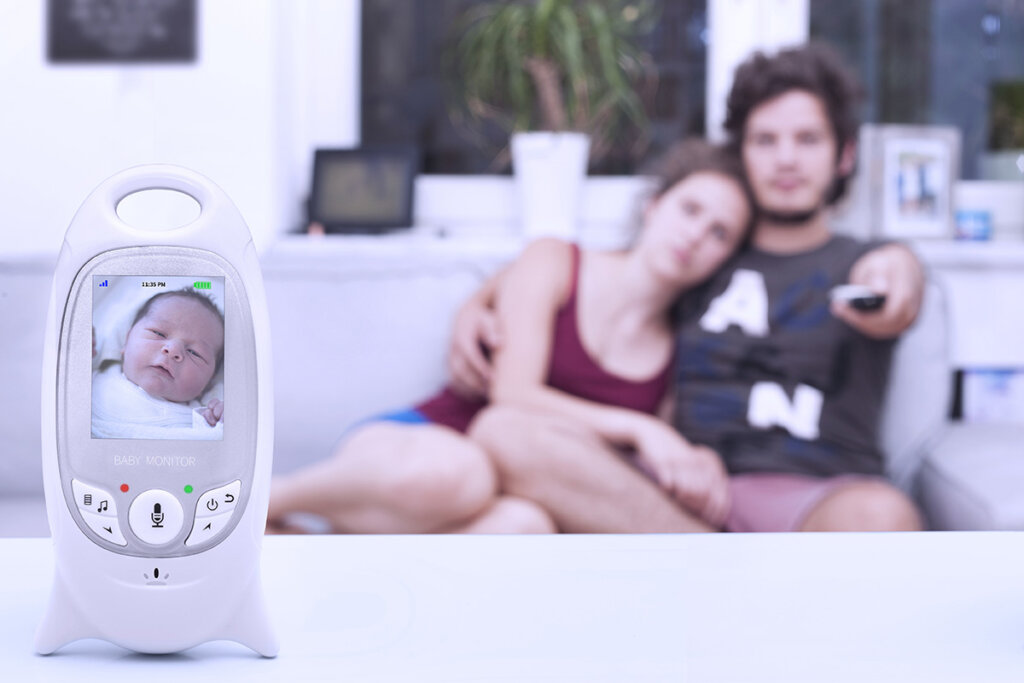 Ungt par som sitter i soffan med en babymonitor framför sig