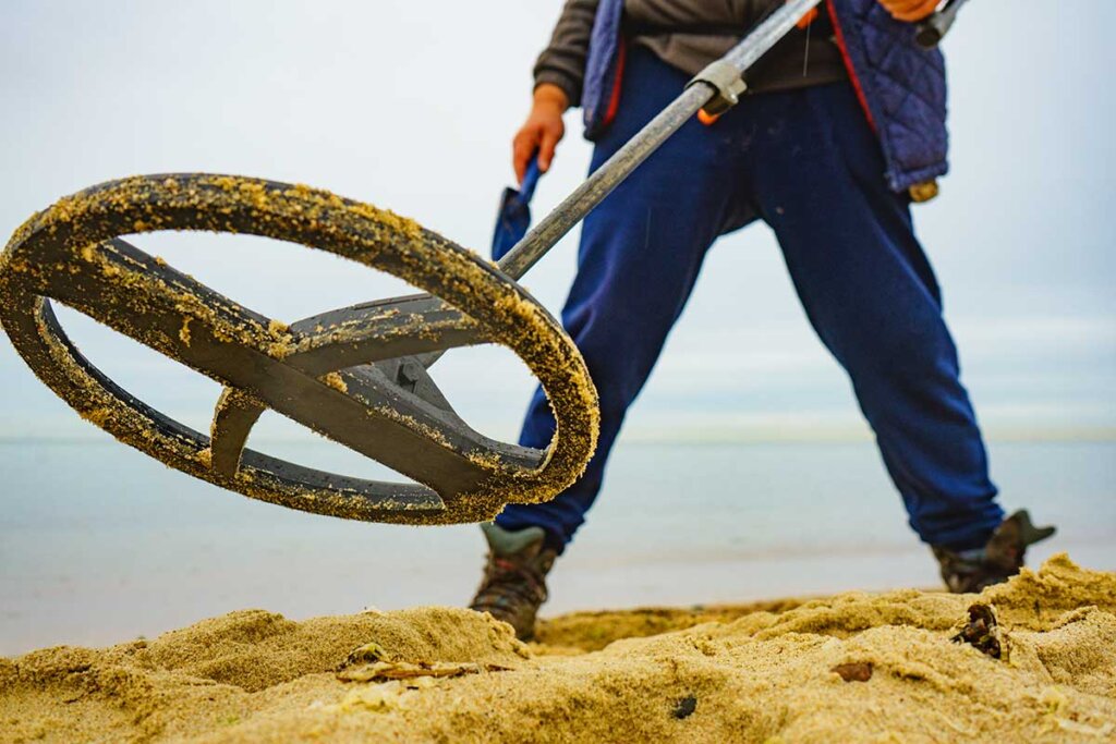 Man står i sand med metalldetektor
