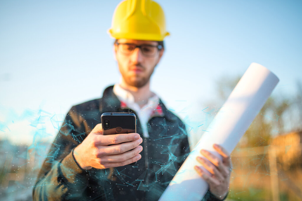 Byggnadsarbetare med hjälm håller en smartphone för utomhusbruk i handen.
