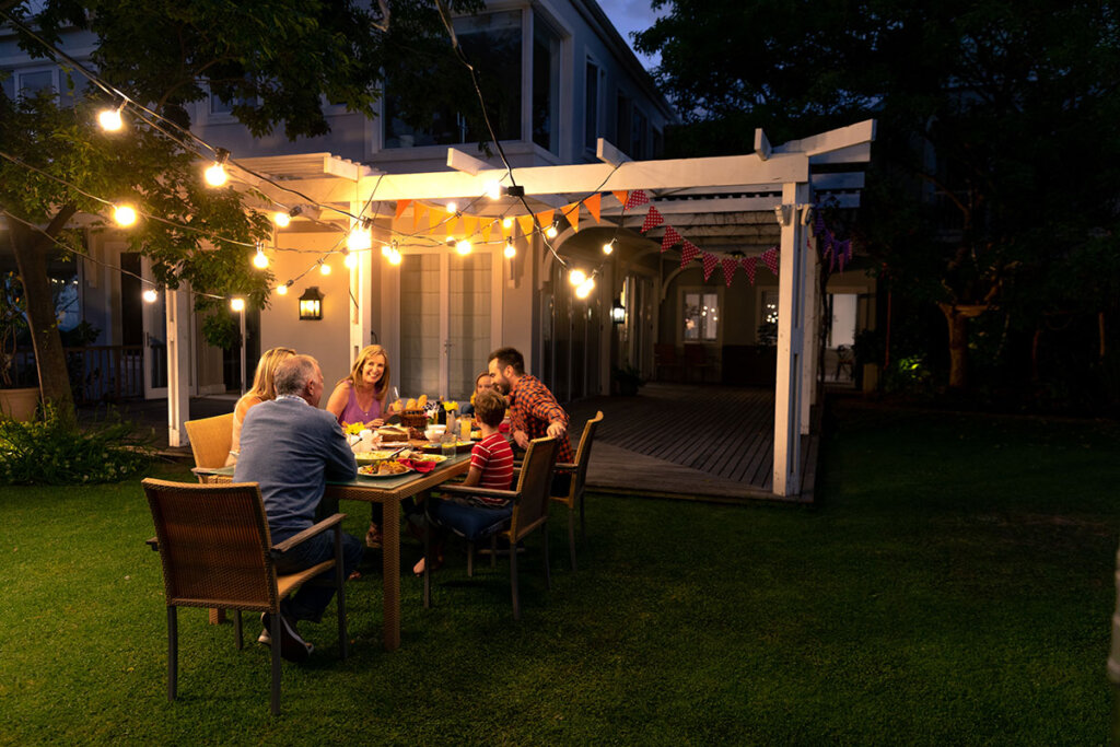 Familjen äter tillsammans i trädgården med ljuskedja.
