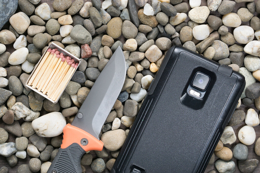 Kniv, tändstickor och smarttelefon på ett grusgolv